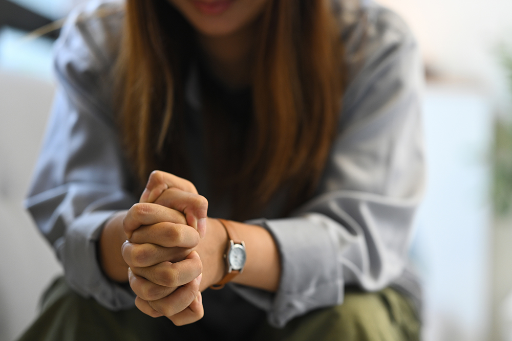Mulher com expressão apreensiva e mãos cruzadas, simbolizando os efeitos da ansiedade na saúde mental e física, incluindo sintomas nas pernas.