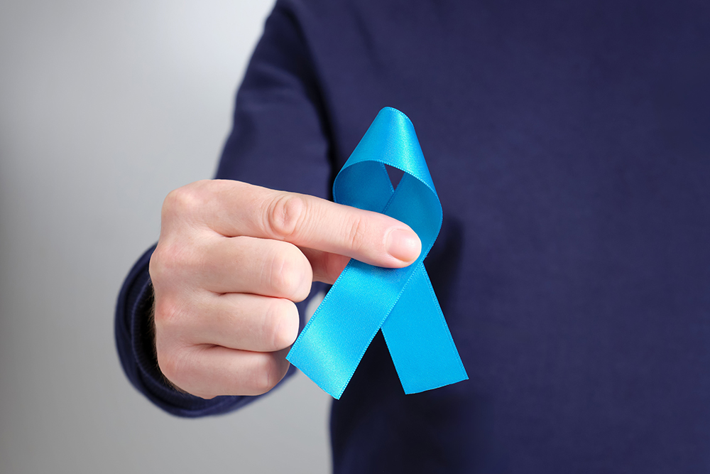 Homem segurando laço azul nas mãos, símbolo da campanha Novembro Azul de conscientização sobre a saúde do homem.