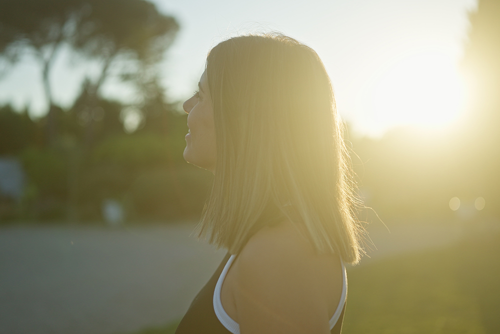 Mulher jovem caminhando ao ar livre ao pôr do sol com expressão de leveza nas pernas e sensação de bem-estar